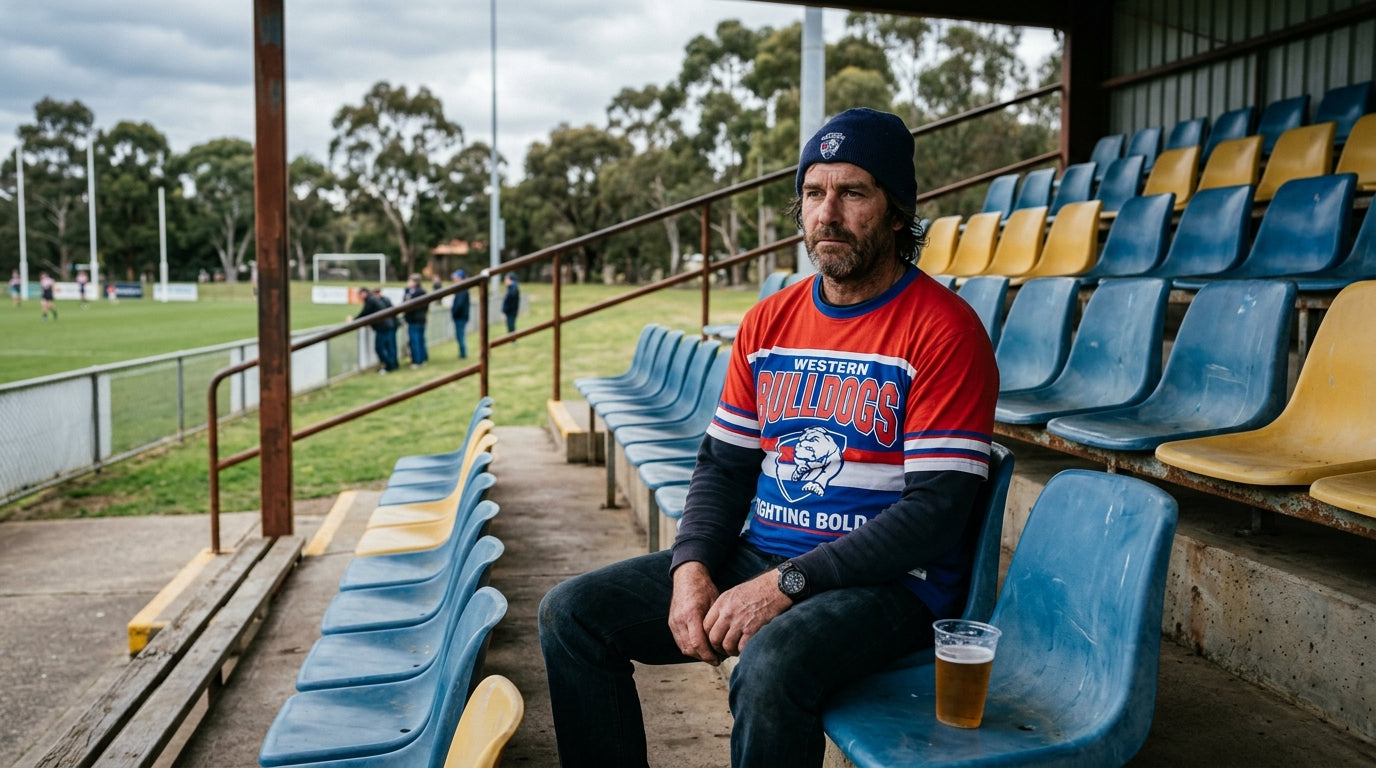 Australian man in AFL graphic tee sitting alone in an empty suburban footy grandstand